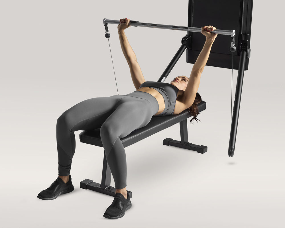 Woman using bar and a Tonal machine on a flat bench performing bench press