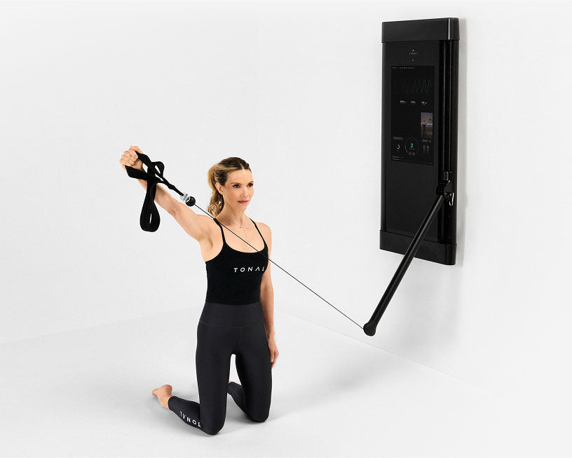 Woman doing workout using Tonal strength training machine and pilates loops