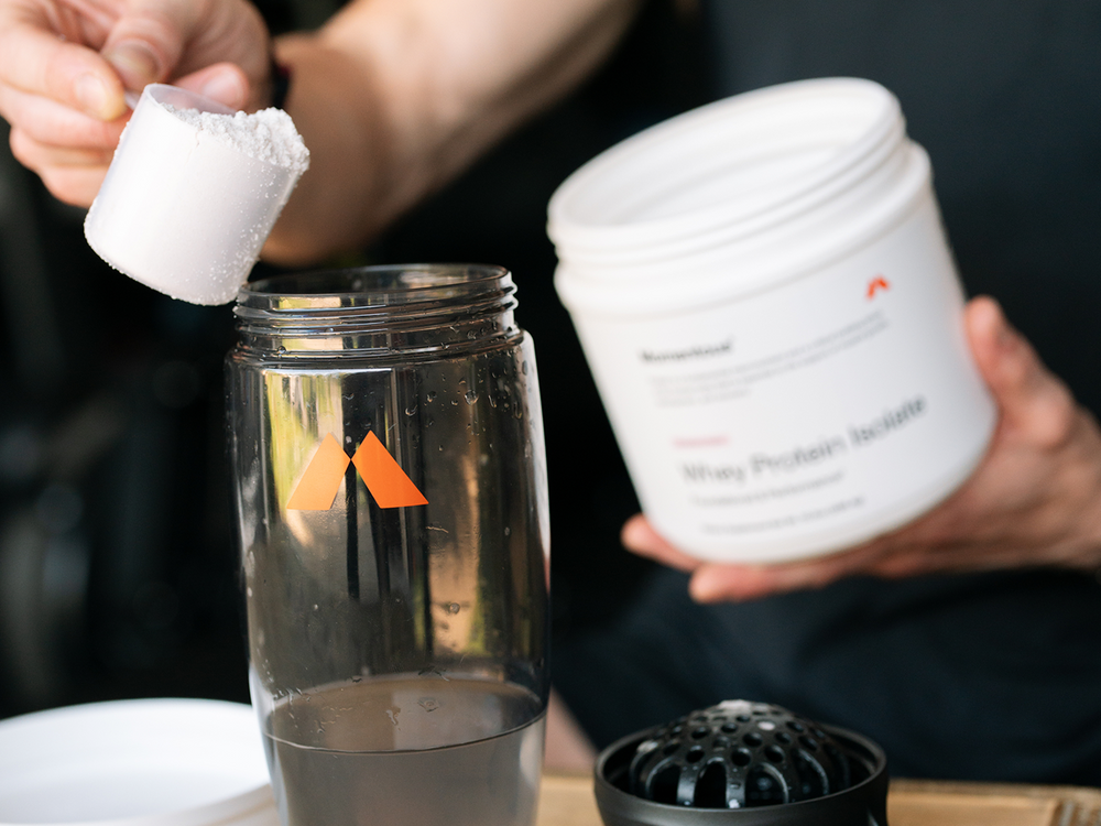 Person adding a Momentous whey protein powder from a container into a blender.
