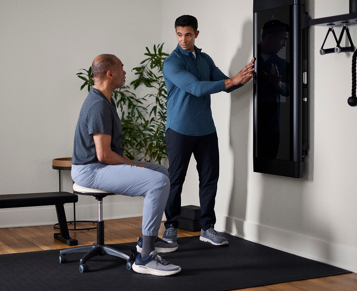Clinician explaining how to use a wall mounted Tonal machine to a patient