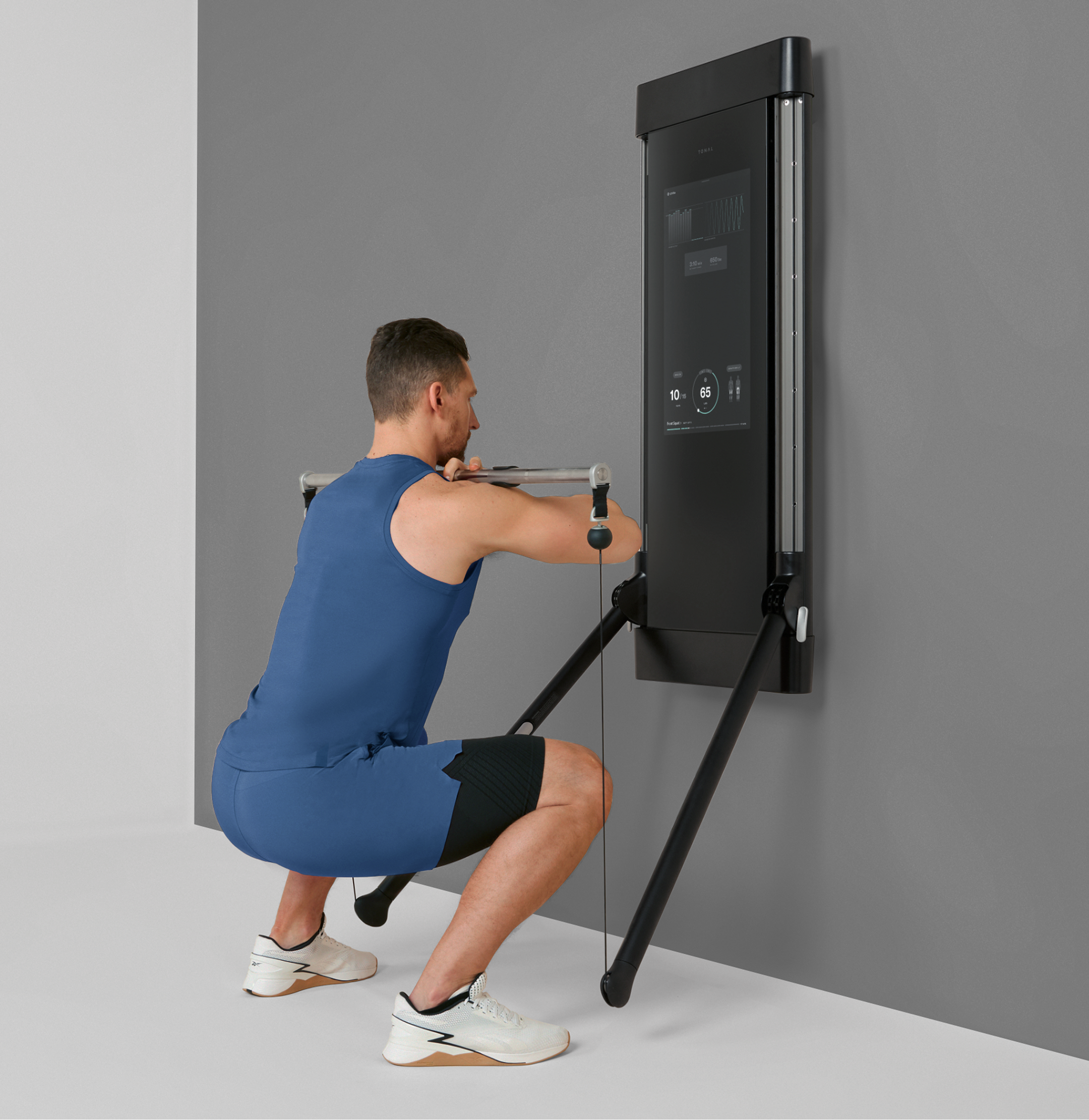 Man using a wall-mounted Tonal to do barbell squats