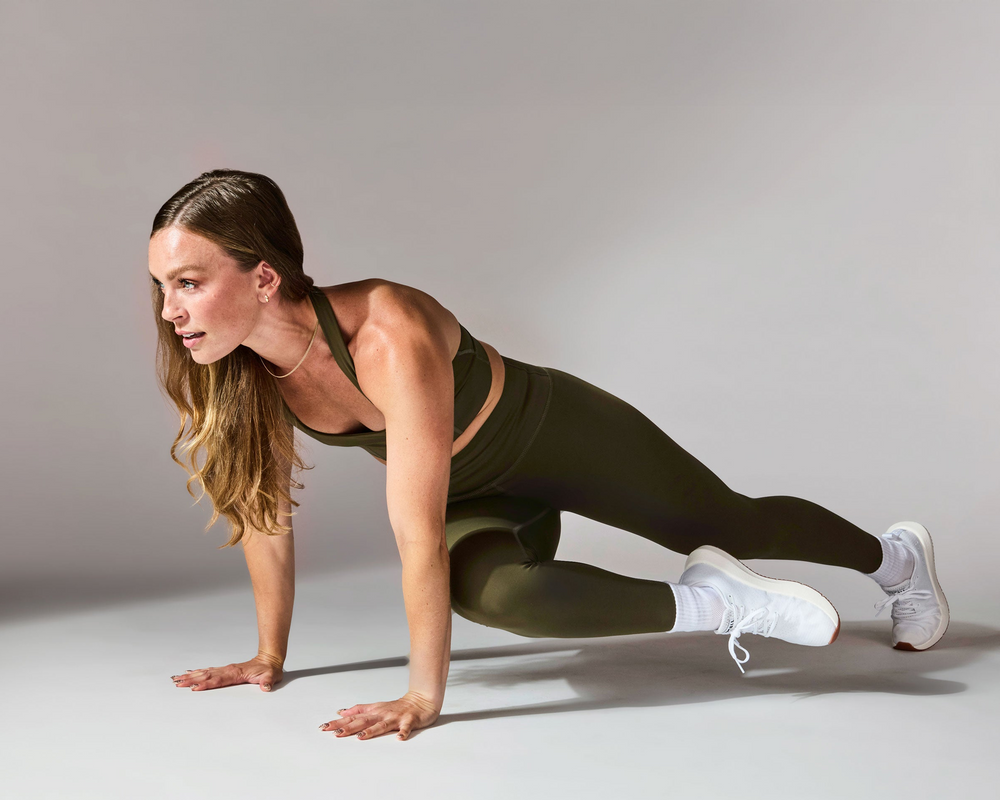 Woman in green athletic wear performing a bodyweight workout on a gray background