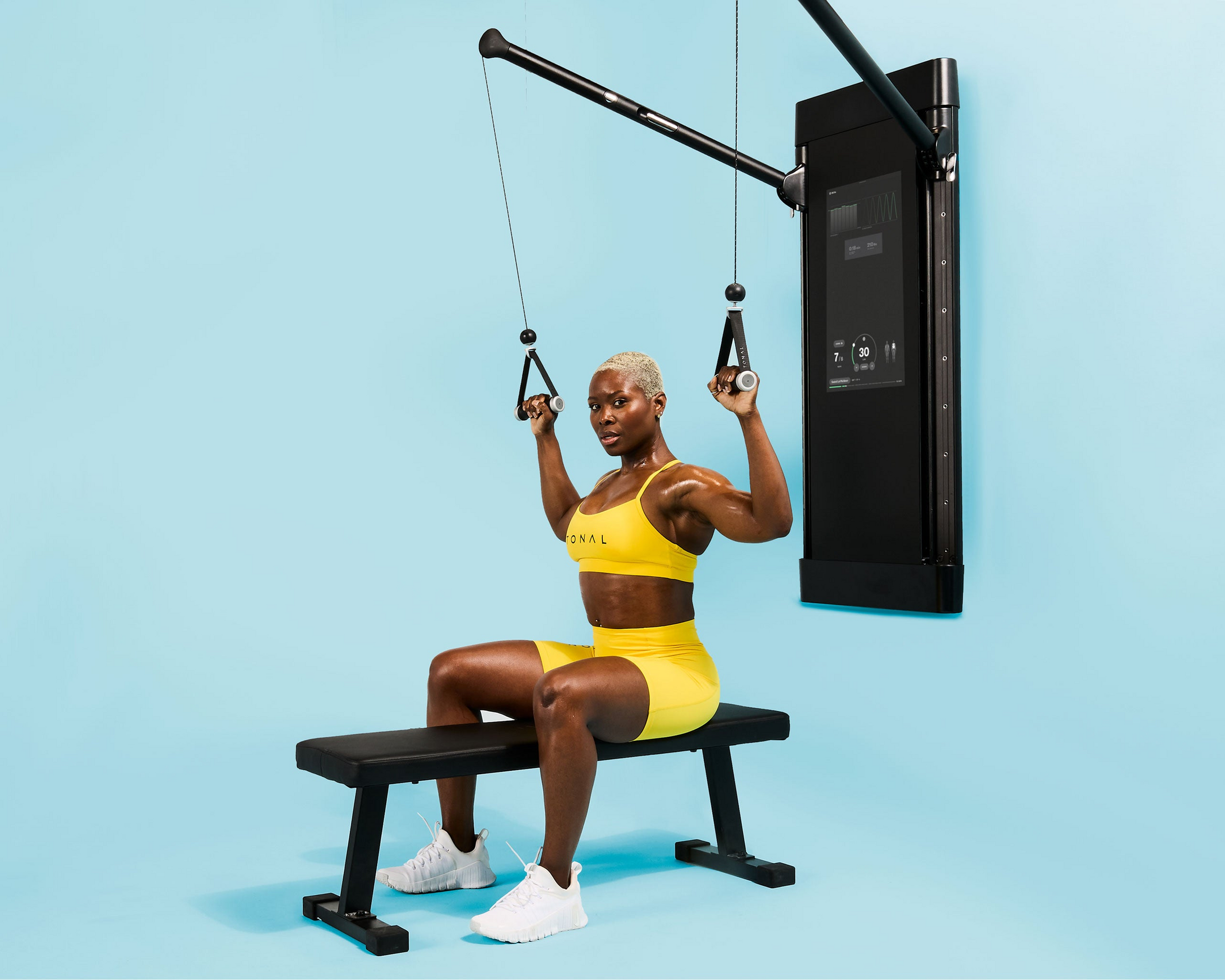 Women using Tonal machine sitting on a flat bench performing a lat pulldown exercise