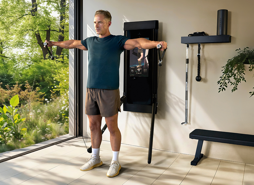 Man exercising using a Tonal home gym machine with a view of greenery outside.